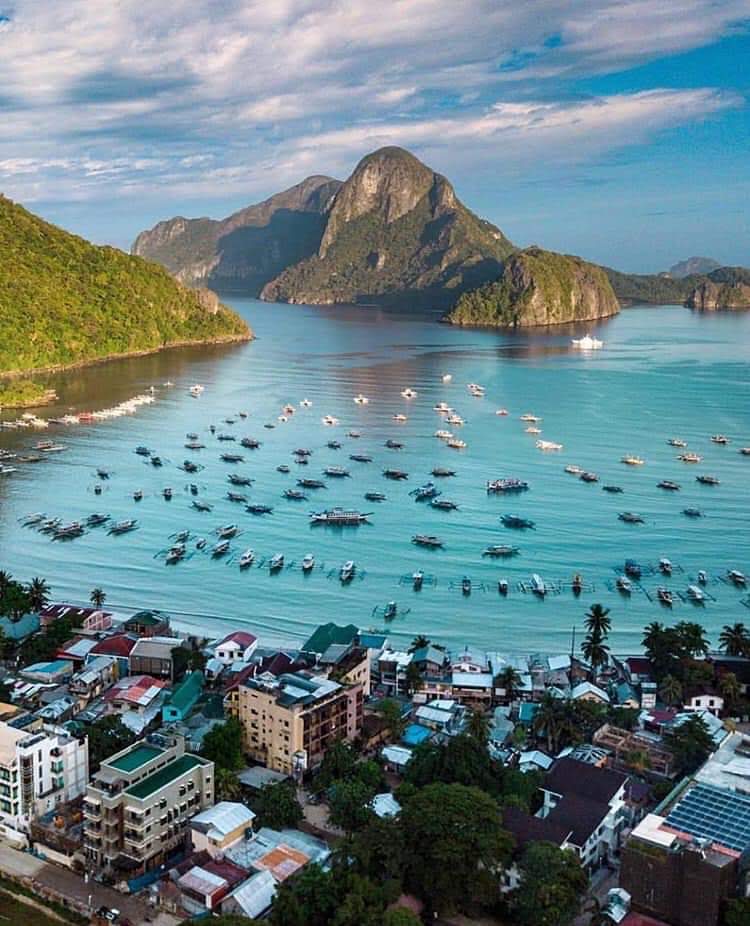 Aerial view of El Nido town and its bay full of outrigger boats, with karst islands behind